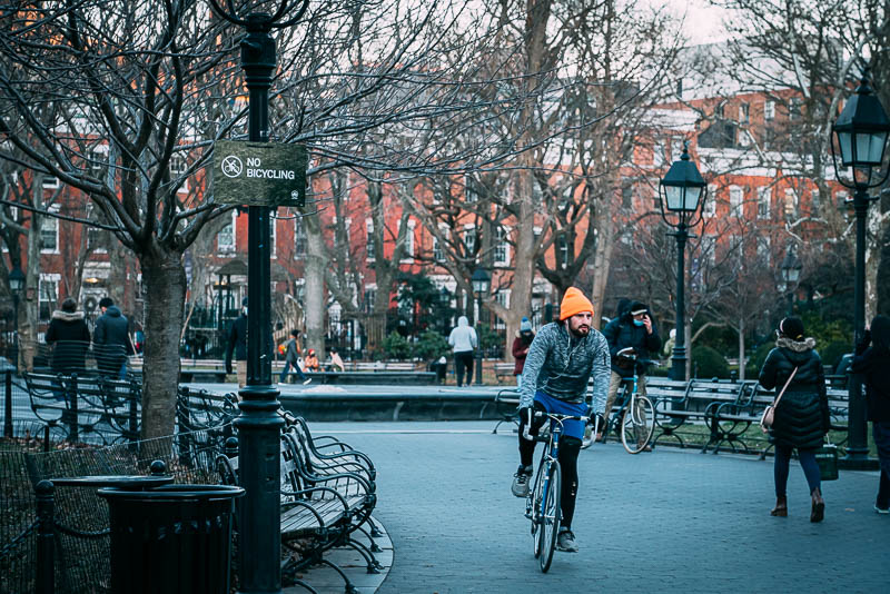 A cyclist in Washington Square Park passing a "No Bicycling" sign